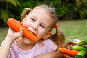 Happy little girl holding and biting carrots
