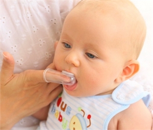 Brushing baby teeth with a finger toothbrushes that fit over the end of the finger. Finger brushes are easy to use with infants and have bristles on one side to clean the teeth and the other side can be used to wipe the gums.
