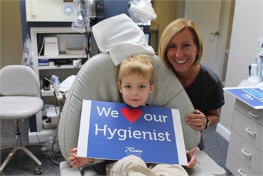 Dental hygienist and patient smiling with sign at Gurnee IL dentist Bradley Rule DDS